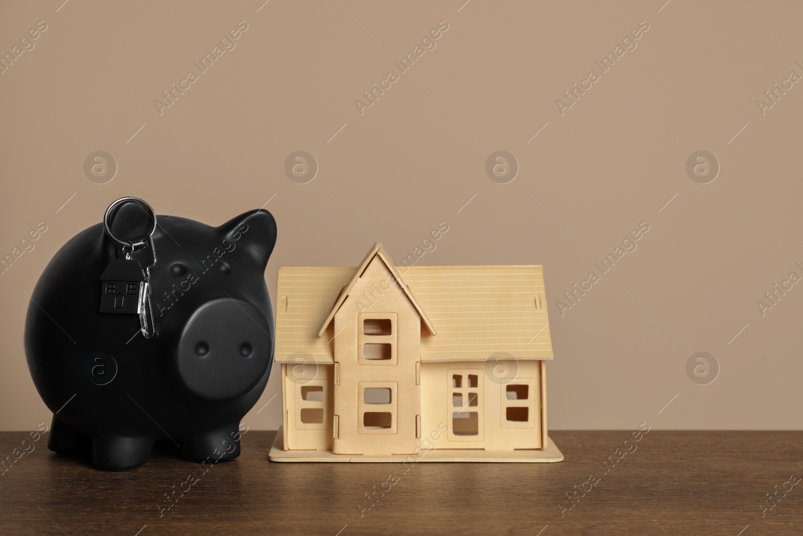 Photo of Piggy bank, keys and house model on wooden table against beige background