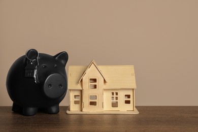 Photo of Piggy bank, keys and house model on wooden table against beige background