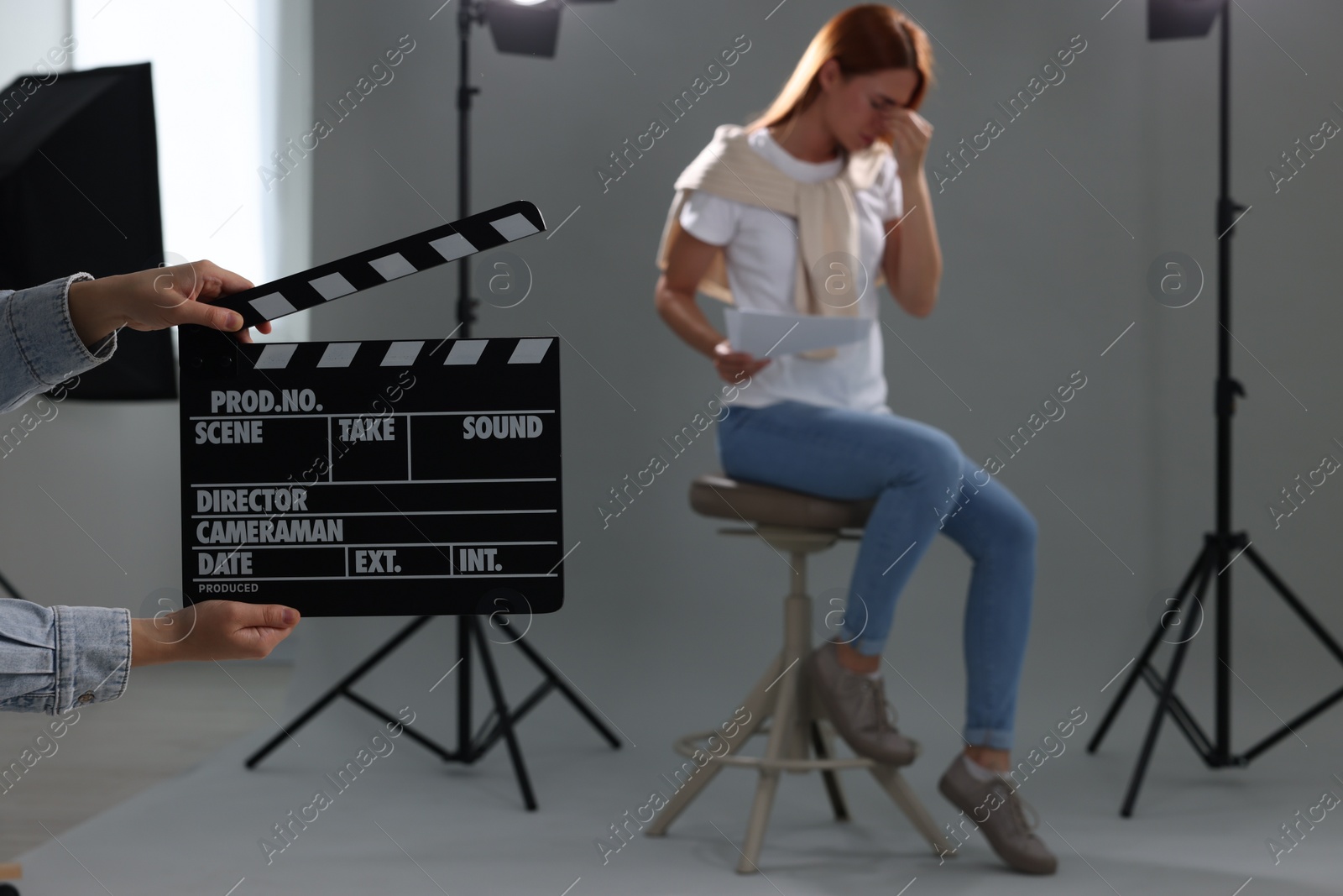 Photo of Casting call. Emotional woman performing while second assistance camera holding clapperboard against grey background in studio, selective focus