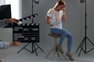 Photo of Casting call. Emotional woman performing while second assistance camera holding clapperboard against grey background in studio, selective focus