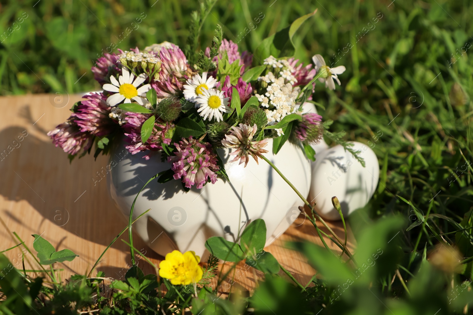 Photo of Ceramic mortar with pestle, different wildflowers and herbs on green grass outdoors, closeup