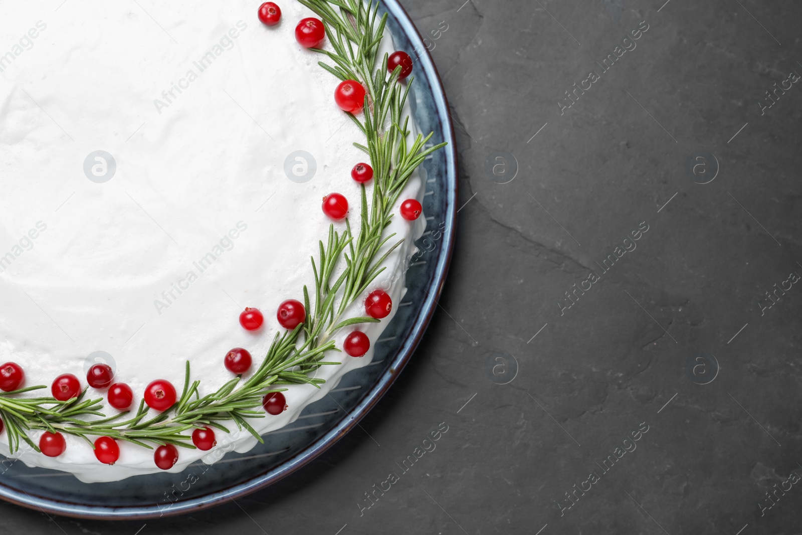 Photo of Traditional Christmas cake decorated with rosemary and cranberries on dark grey table, top view