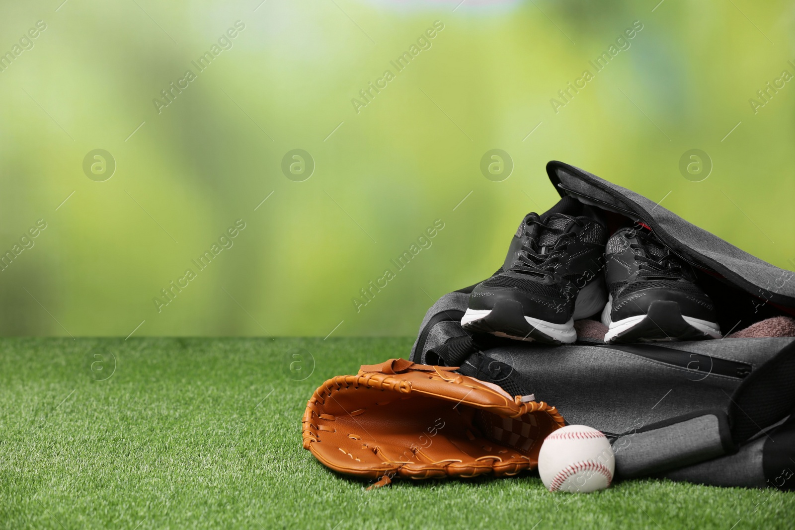 Photo of Bag and different sports equipment on grass against blurred background. Space for text