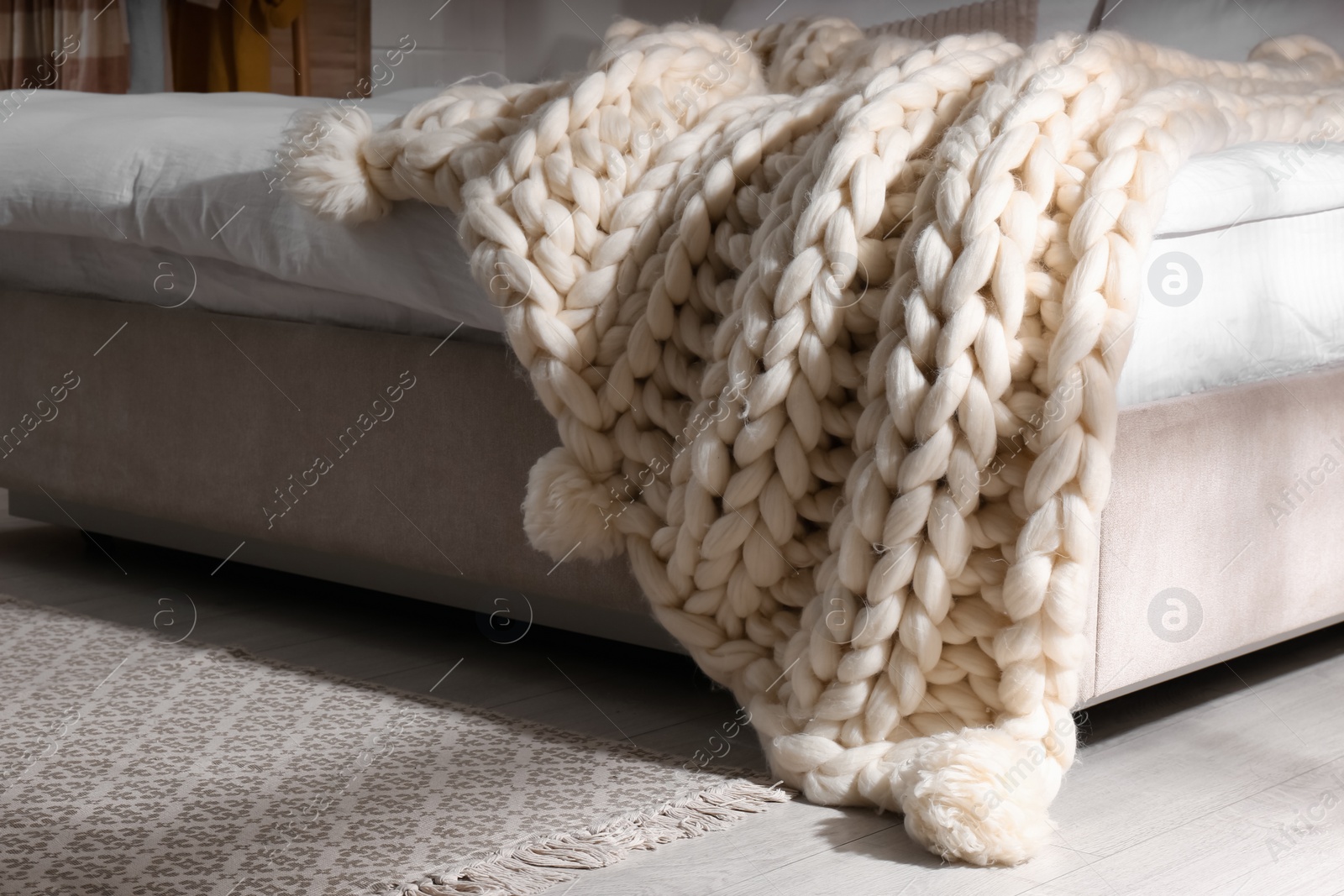 Photo of Bed with white knitted plaid indoors. Interior design