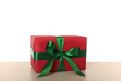 Red gift box with green bow on wooden table against white background