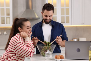 Photo of Happy lovely couple cooking together near laptop in kitchen