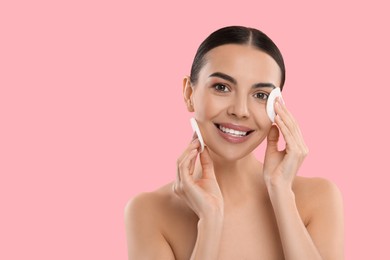 Beautiful woman removing makeup with cotton pads on pink background, space for text