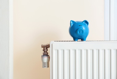 Photo of Piggy bank on modern heating radiator indoors