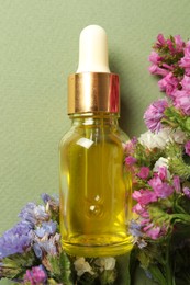 Bottle of face serum with beautiful flowers on light green background, top view