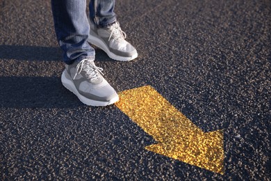 Planning future. Man walking to drawn mark on road, closeup. Yellow arrow showing direction of way