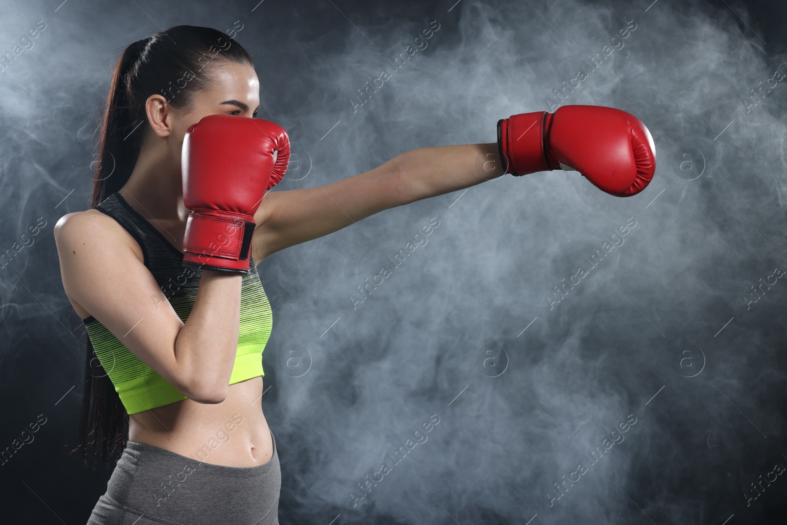 Photo of Woman wearing boxing gloves training in smoke on black background. Space for text