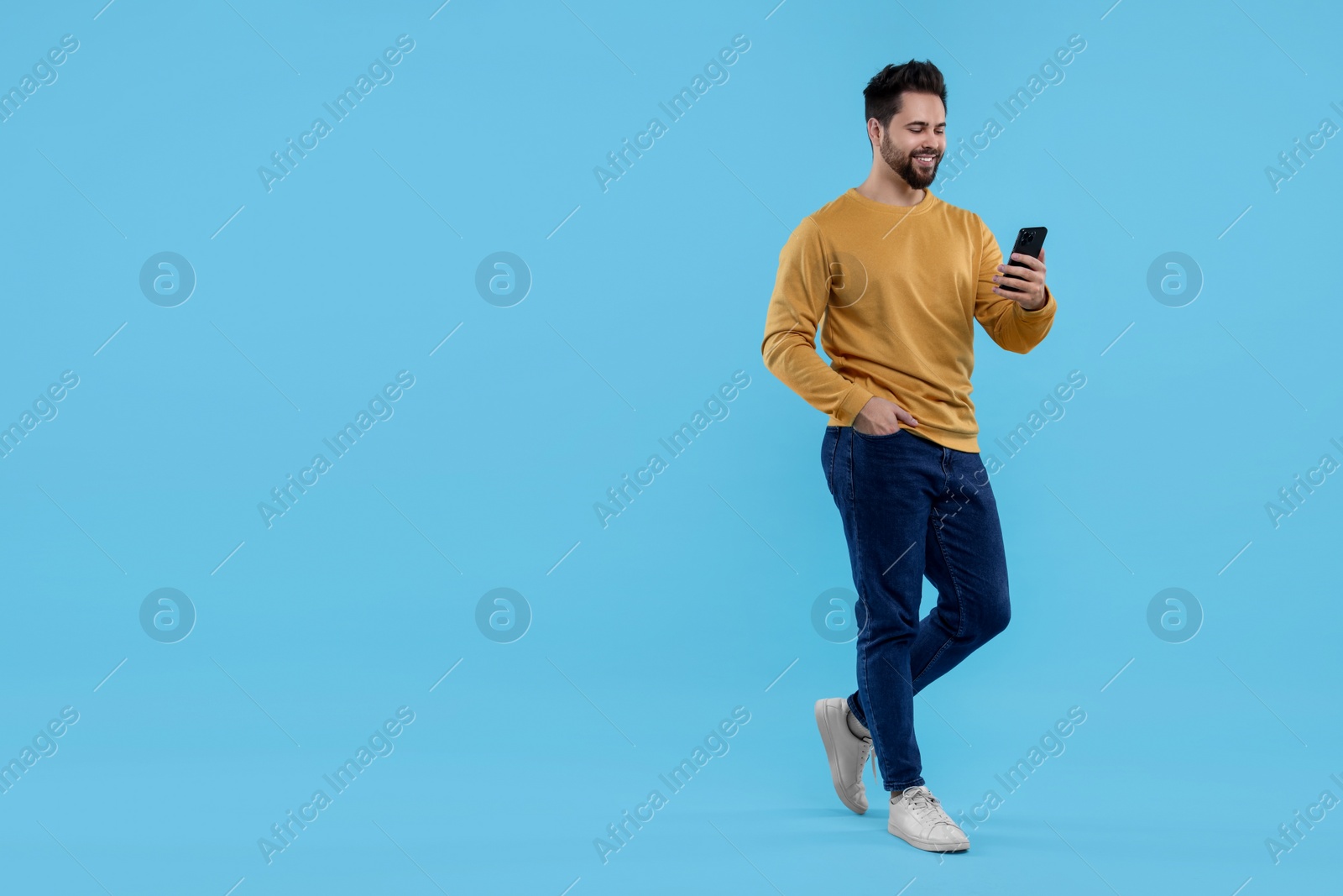 Photo of Happy young man using smartphone on light blue background, space for text