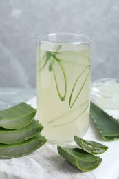 Photo of Tasty aloe juice in glass and cut fresh leaves on light grey table, closeup