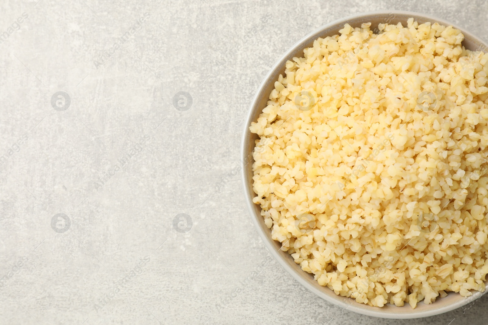 Photo of Delicious bulgur in bowl on gray table, top view. Space for text