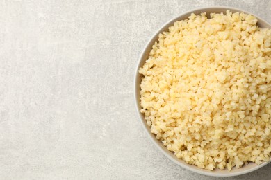 Photo of Delicious bulgur in bowl on gray table, top view. Space for text