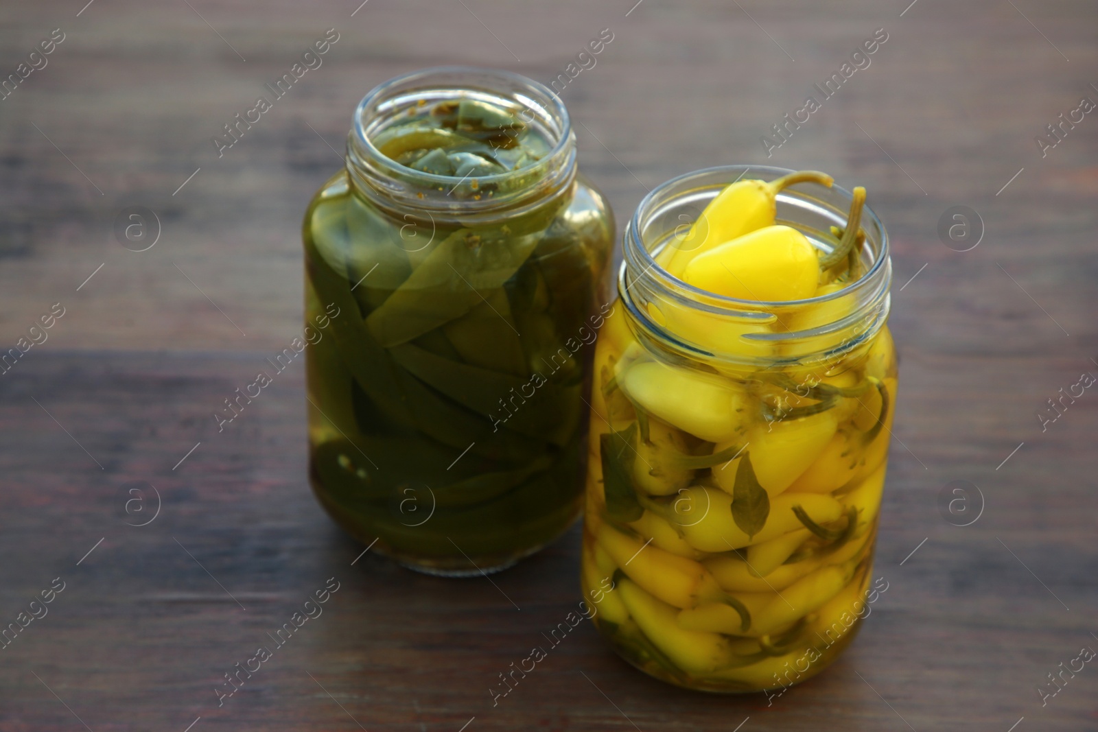 Photo of Glass jars of pickled green and yellow jalapeno peppers on wooden table