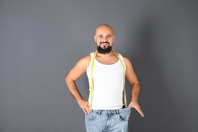 Photo of Overweight man with measuring tape wearing oversized pants on gray background