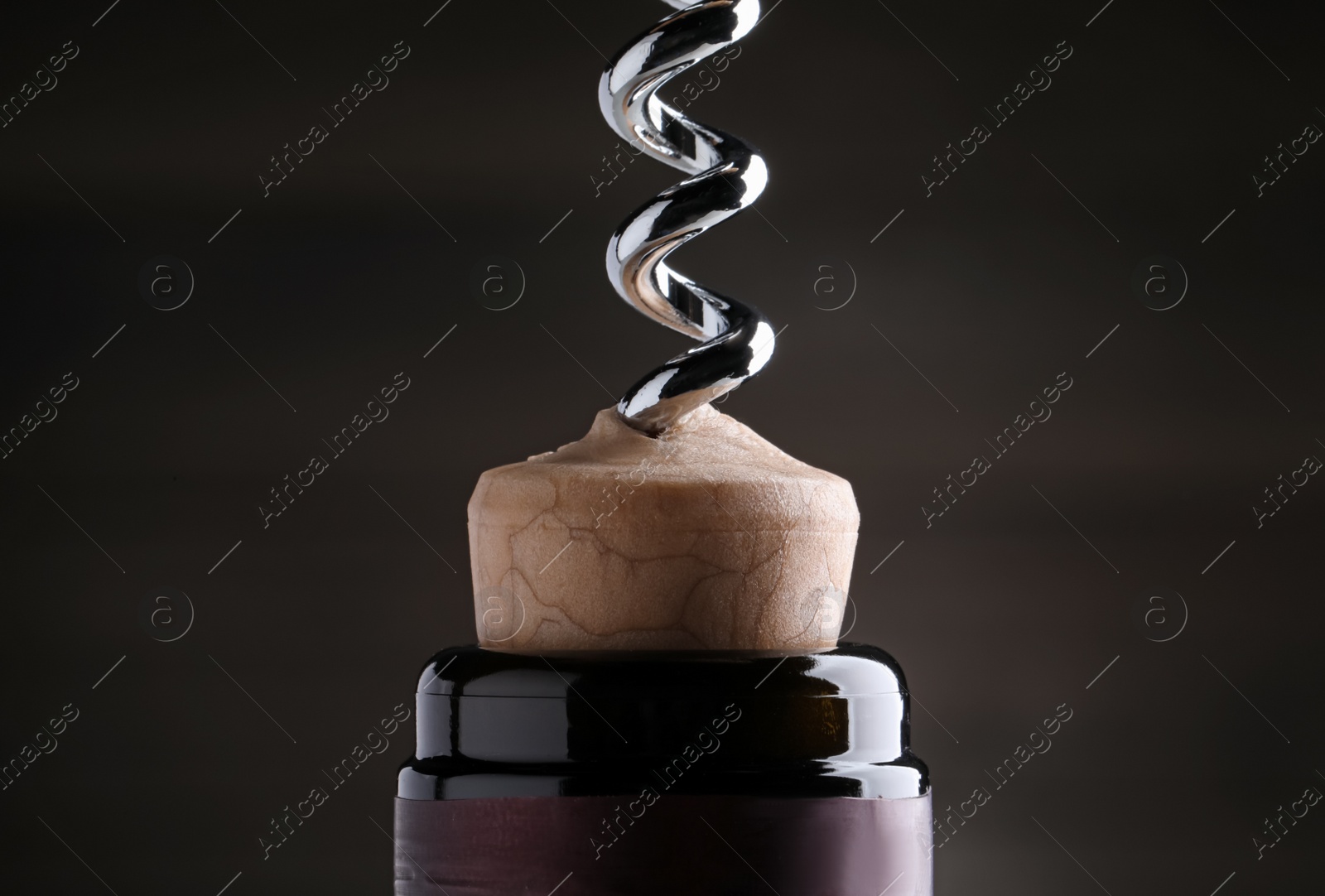 Photo of Opening wine bottle with corkscrew on dark background, closeup