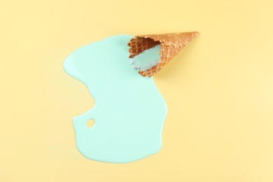 Melted ice cream and wafer cone on beige background, top view