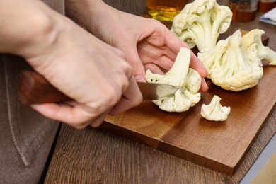 Photo of Woman cutting fresh cauliflower at wooden table, closeup