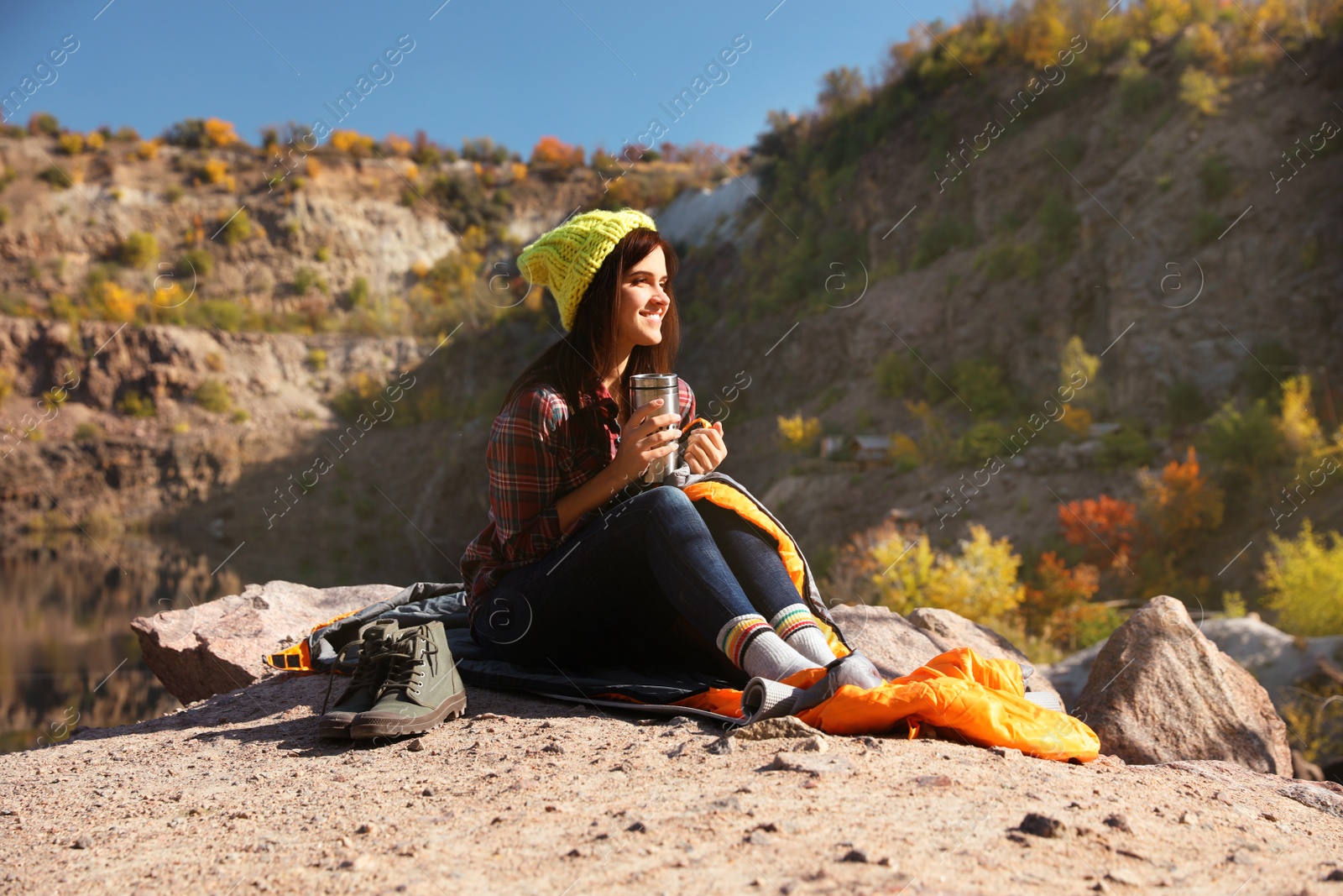 Photo of Female camper with thermos sitting on sleeping bag in wilderness