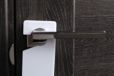 Photo of Closed wooden door with blank hanger on metal handle, closeup