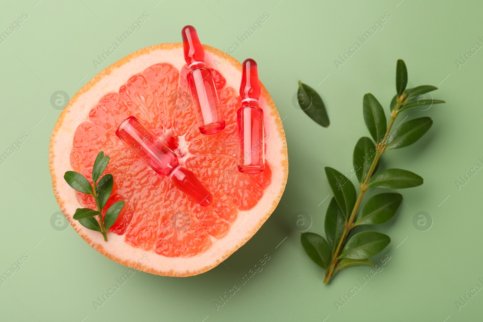 Photo of Skincare ampoules with vitamin C, half of grapefruit and leaves on light green background, flat lay