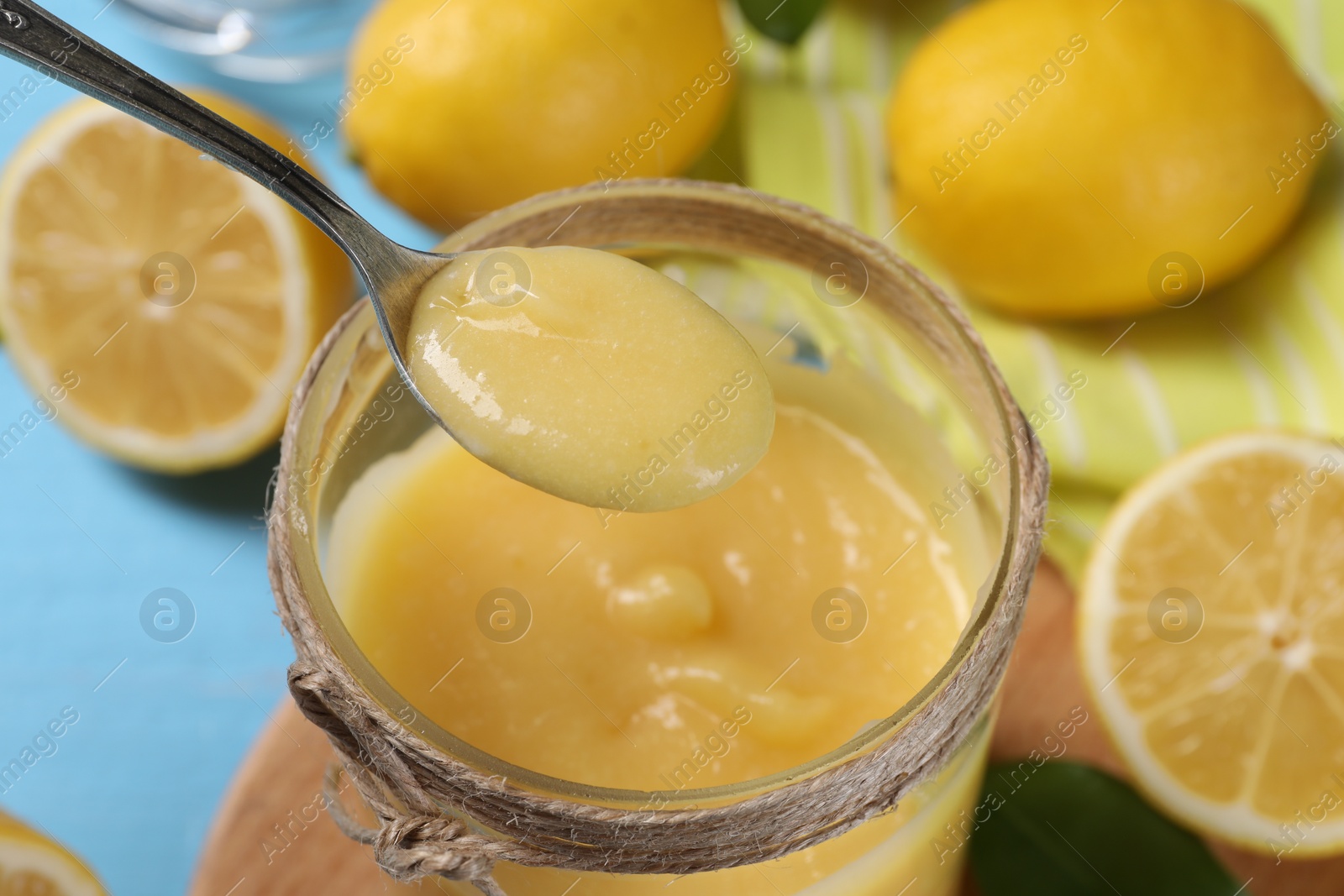 Photo of Taking delicious lemon curd from jar at light blue table, closeup