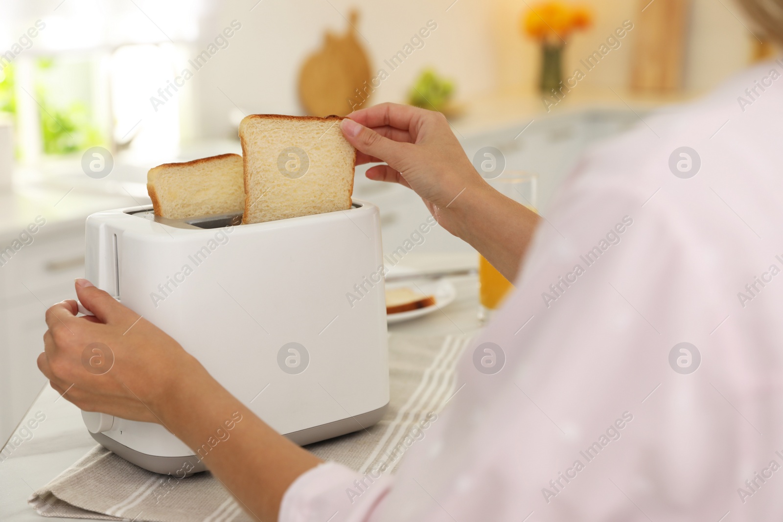 Photo of Young woman using toaster at table in kitchen, closeup