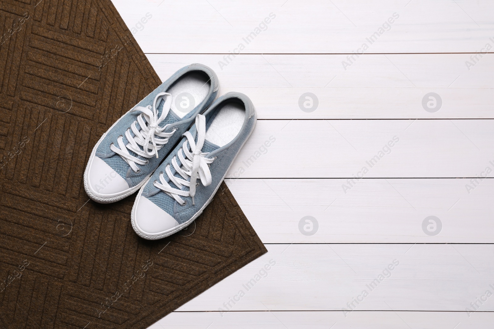 Photo of New clean door mat with shoes on white wooden floor, flat lay. Space for text