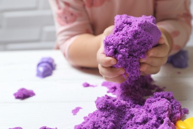 Photo of Little child playing with kinetic sand at white table, closeup