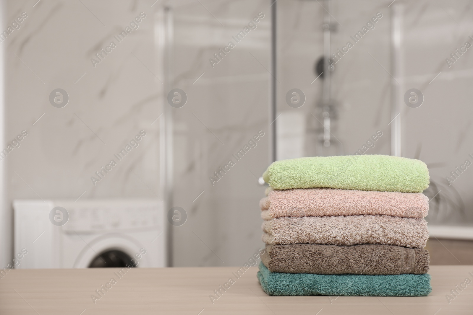 Photo of Stack of fresh towels on wooden table in bathroom. Space for text