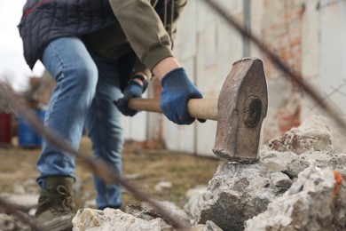 Photo of Man breaking stones with sledgehammer outdoors, closeup