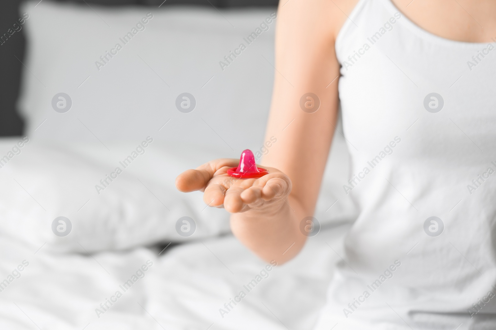 Photo of Woman holding unpacked condom on bed, closeup. Safe sex