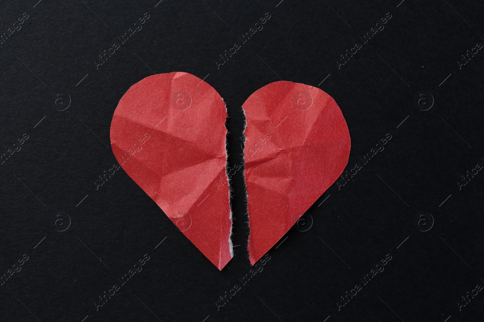 Photo of Halves of torn paper heart on black background, top view. Breakup concept