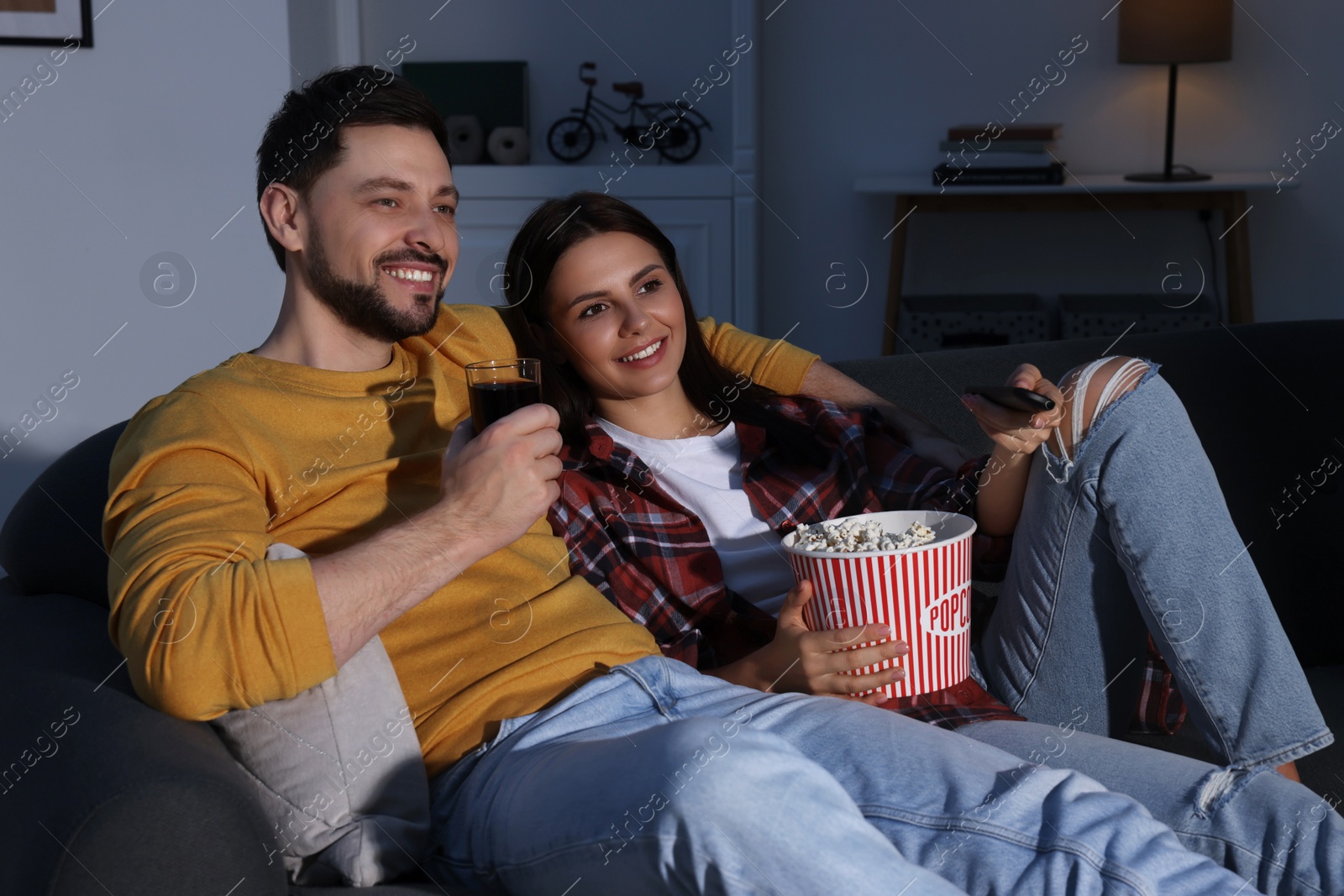 Photo of Happy couple with popcorn watching TV at home in evening