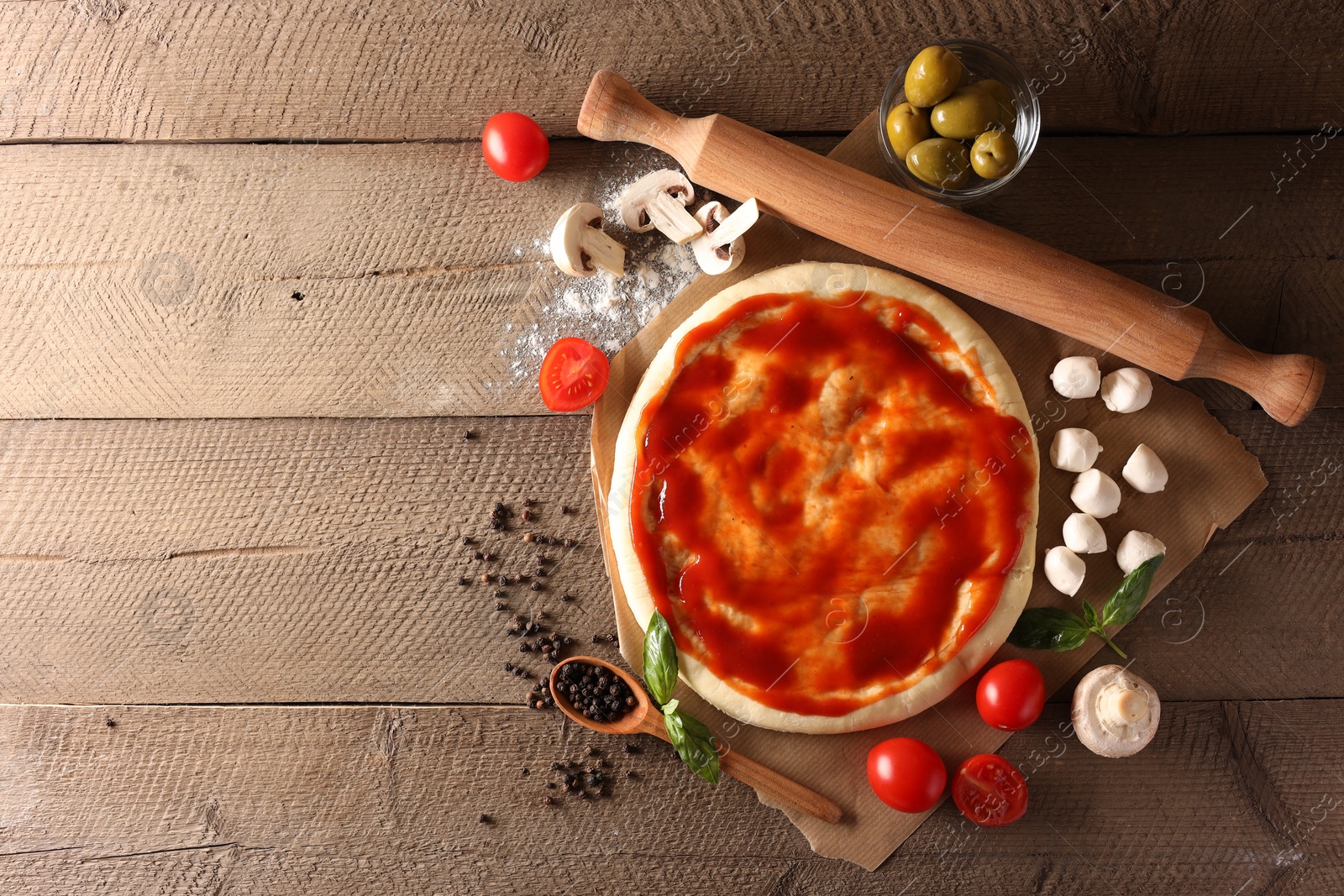 Photo of Pizza dough smeared with tomato sauce, products and rolling pin on wooden table, flat lay. Space for text