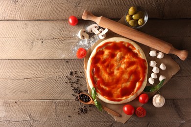 Photo of Pizza dough smeared with tomato sauce, products and rolling pin on wooden table, flat lay. Space for text