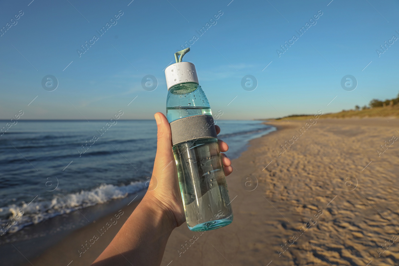 Photo of Woman holding glass bottle with water near sea, closeup