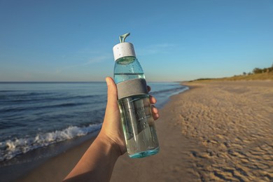 Photo of Woman holding glass bottle with water near sea, closeup