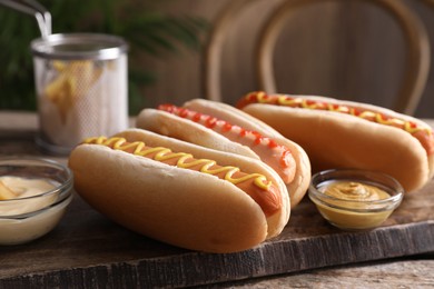 Delicious hot dogs with sauces on wooden table, closeup