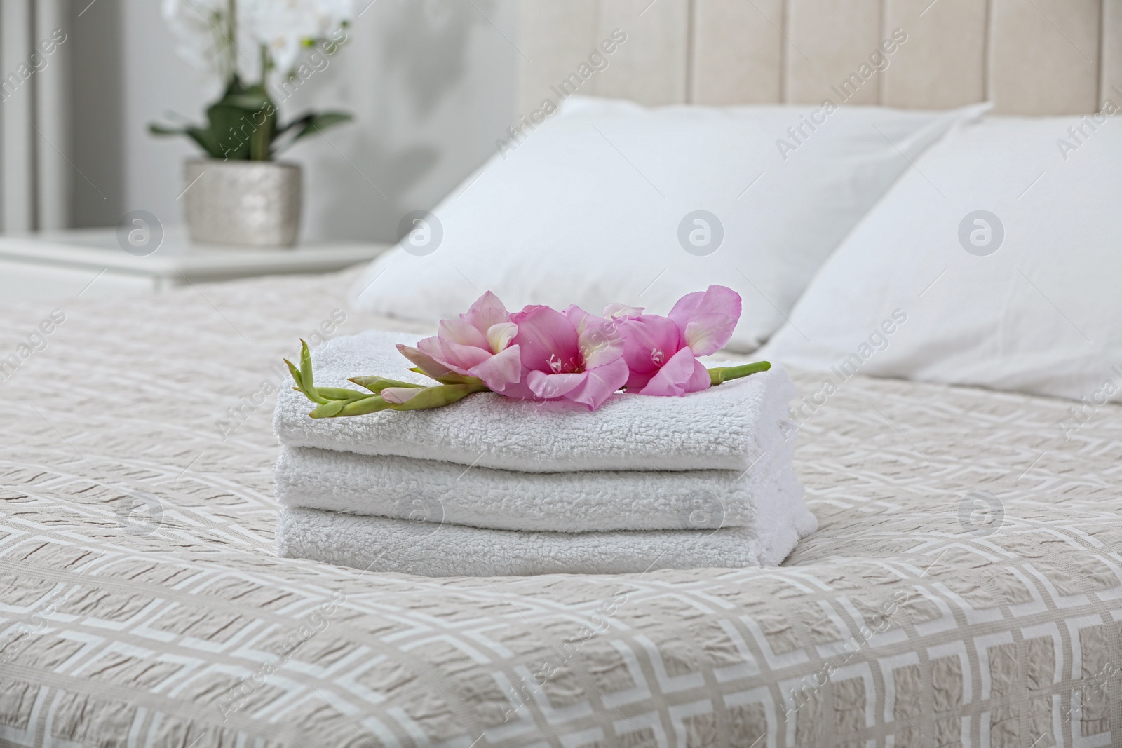 Photo of Stack of clean towels and gladiolus flowers on bed indoors