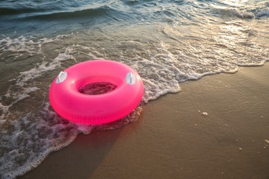 Bright pink inflatable ring on sandy beach near sea, space for text
