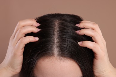 Woman examining her hair and scalp on beige background, closeup
