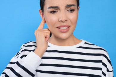 Young woman suffering from ear pain on light blue background, closeup