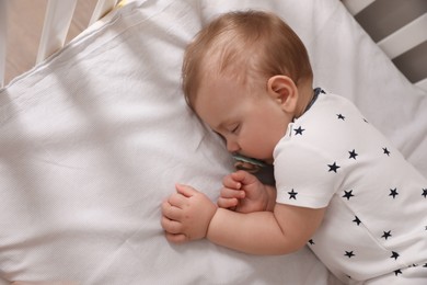 Photo of Adorable little baby with pacifier sleeping in crib, above view