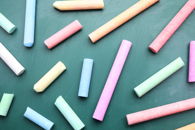 Photo of Pieces of color chalk on greenboard, flat lay