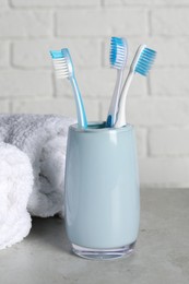 Photo of Plastic toothbrushes in holder and towels on light grey table