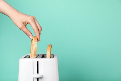 Photo of Woman taking bread slice out of toaster on turquoise background, closeup. Space for text