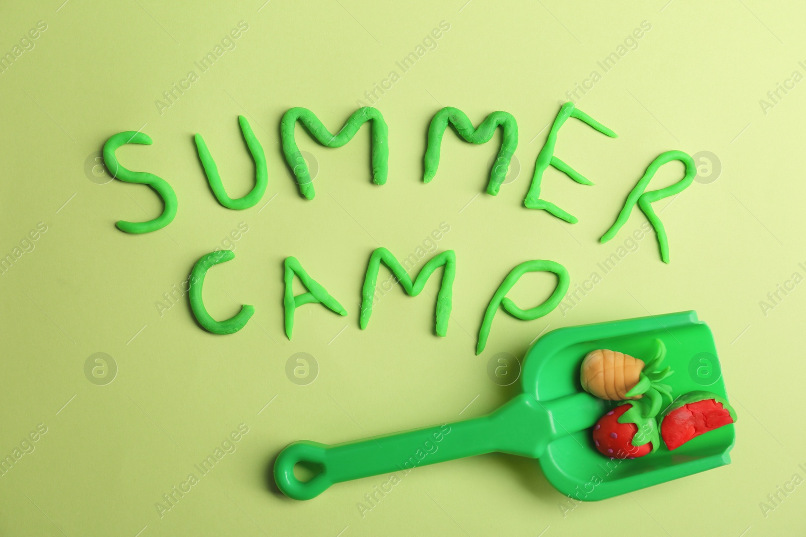 Photo of Flat lay composition with words SUMMER CAMP made from modelling clay and plastic shovel on color background